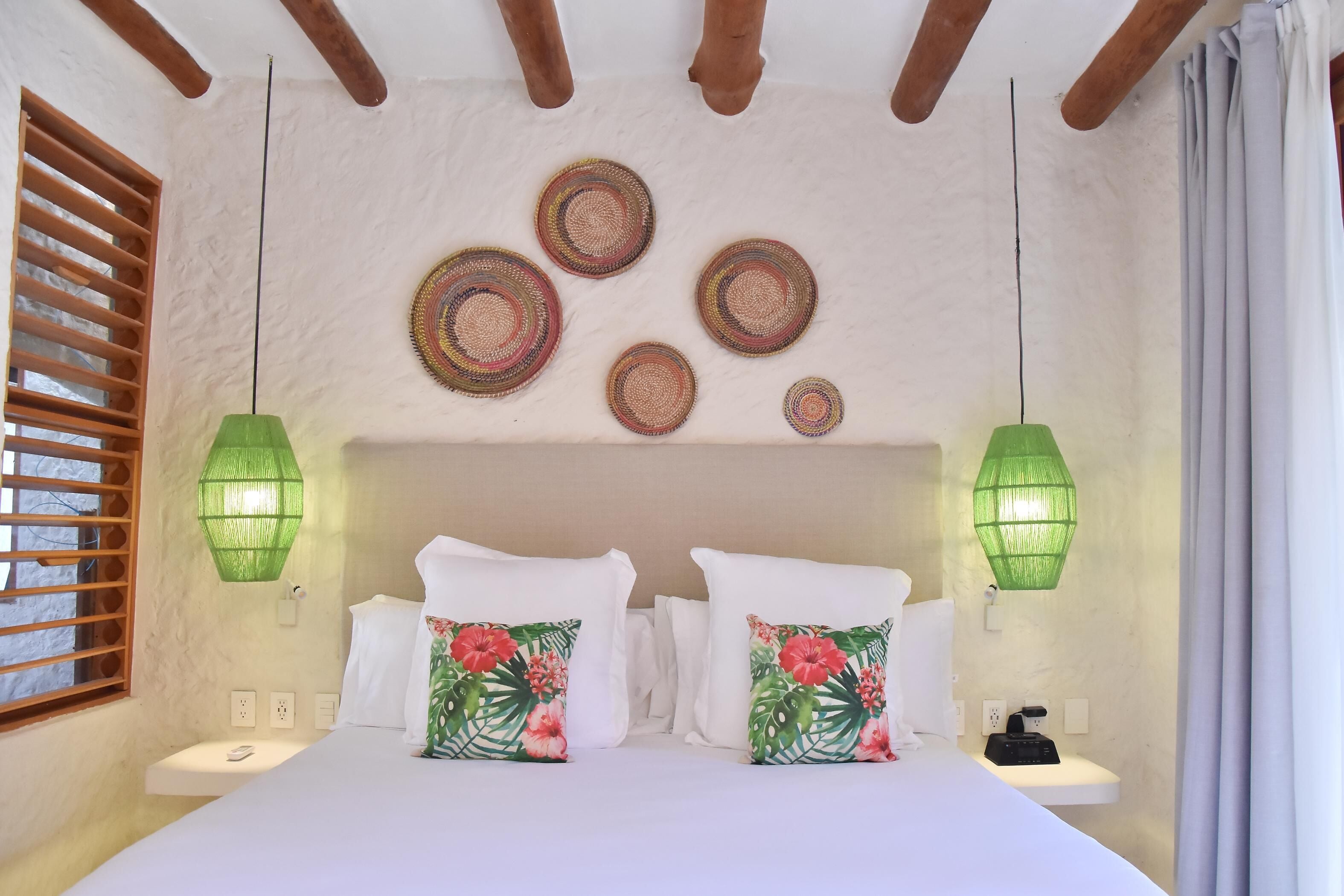 A bedroom with a bed, two nightstands, a wall-mounted lamp, and a window with wooden blinds.