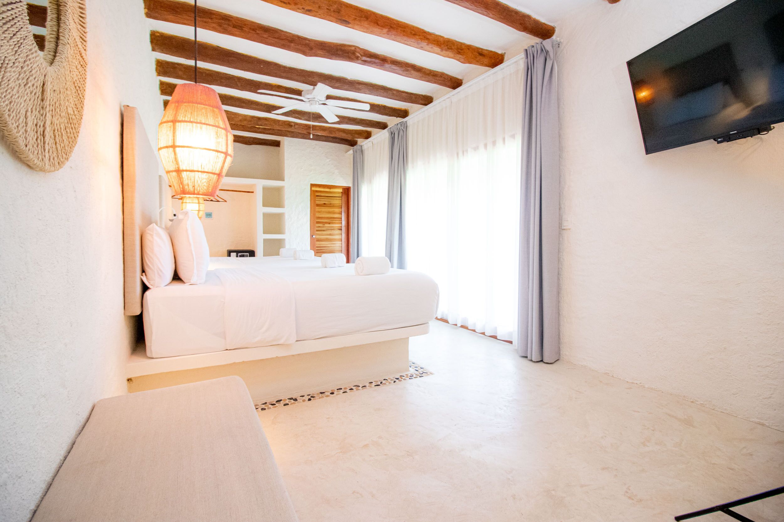 Une chambre à coucher avec un lit, un ventilateur de plafond, une télévision et une fenêtre avec des rideaux.