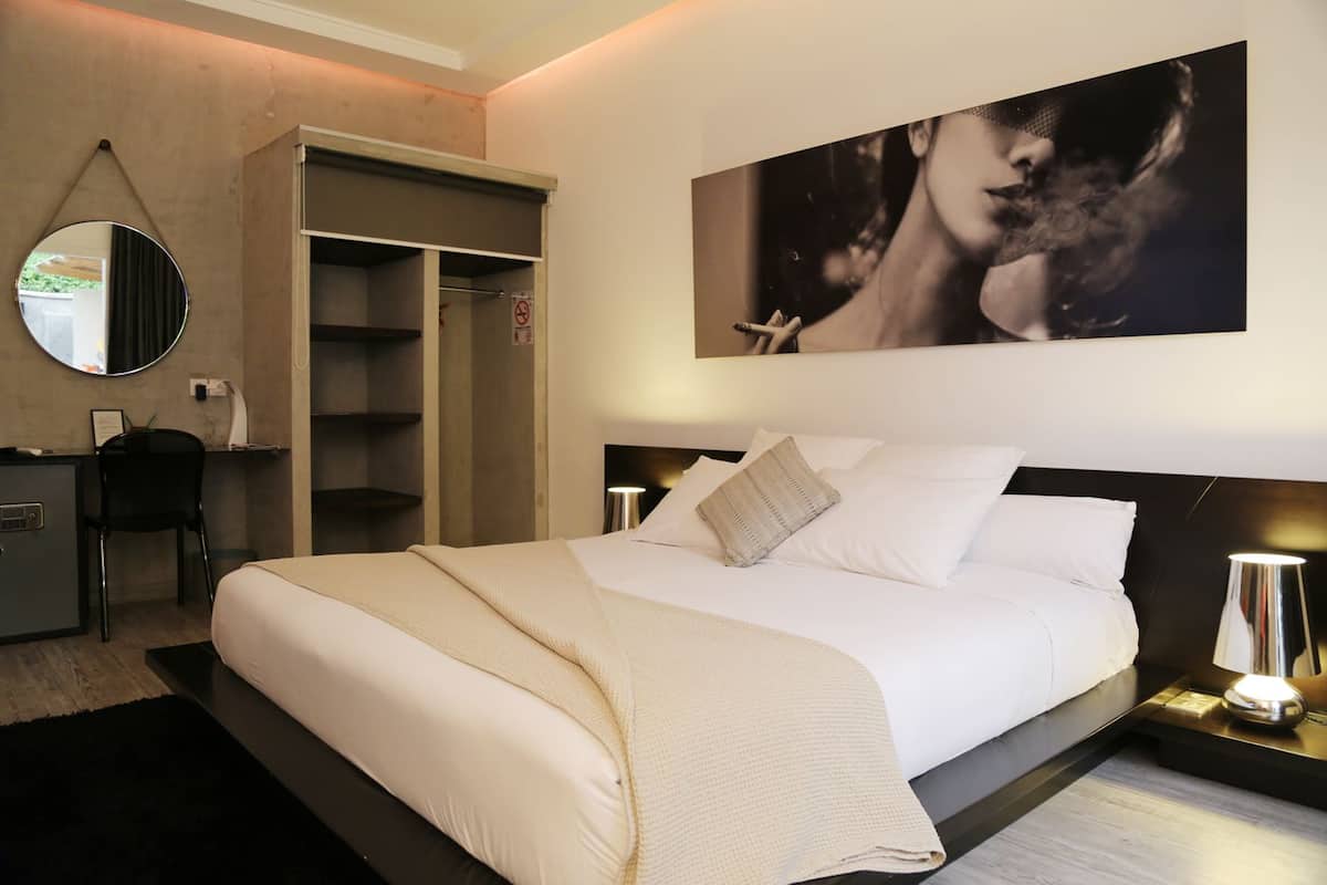 A modern bedroom with a large bed, a wardrobe, a desk, and a mirror.