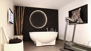 A modern bathroom with a freestanding bathtub, a treadmill, and a large mirror. - Le Stanislas Maison d'Hôtes (Abidjan)