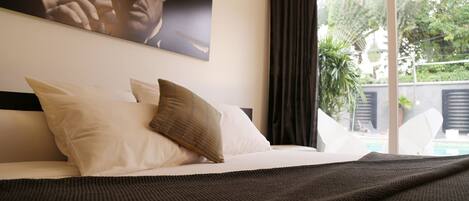A bedroom with a large bed, a view of the outdoors, and a painting on the wall.