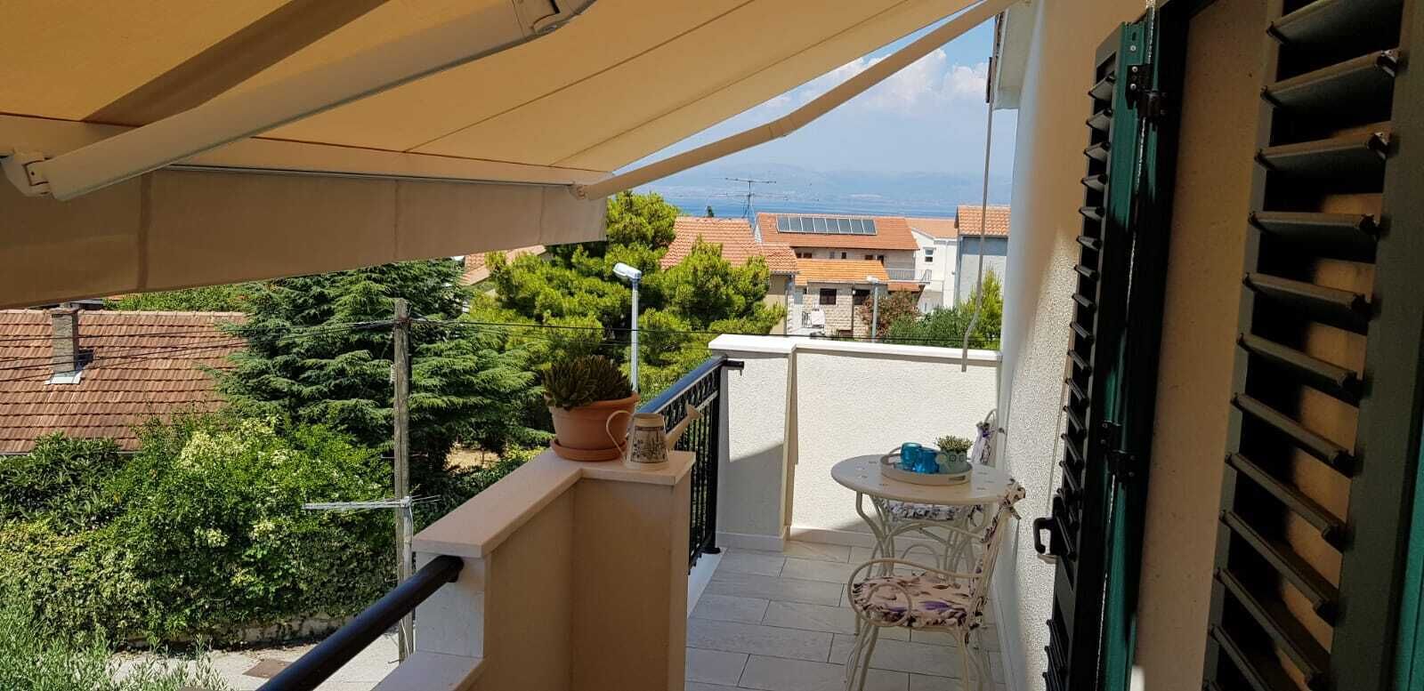 Ein Balkon mit einem Blumentopf, einem Tisch und einem Stuhl sowie Blick auf Gebäude und Bäume.