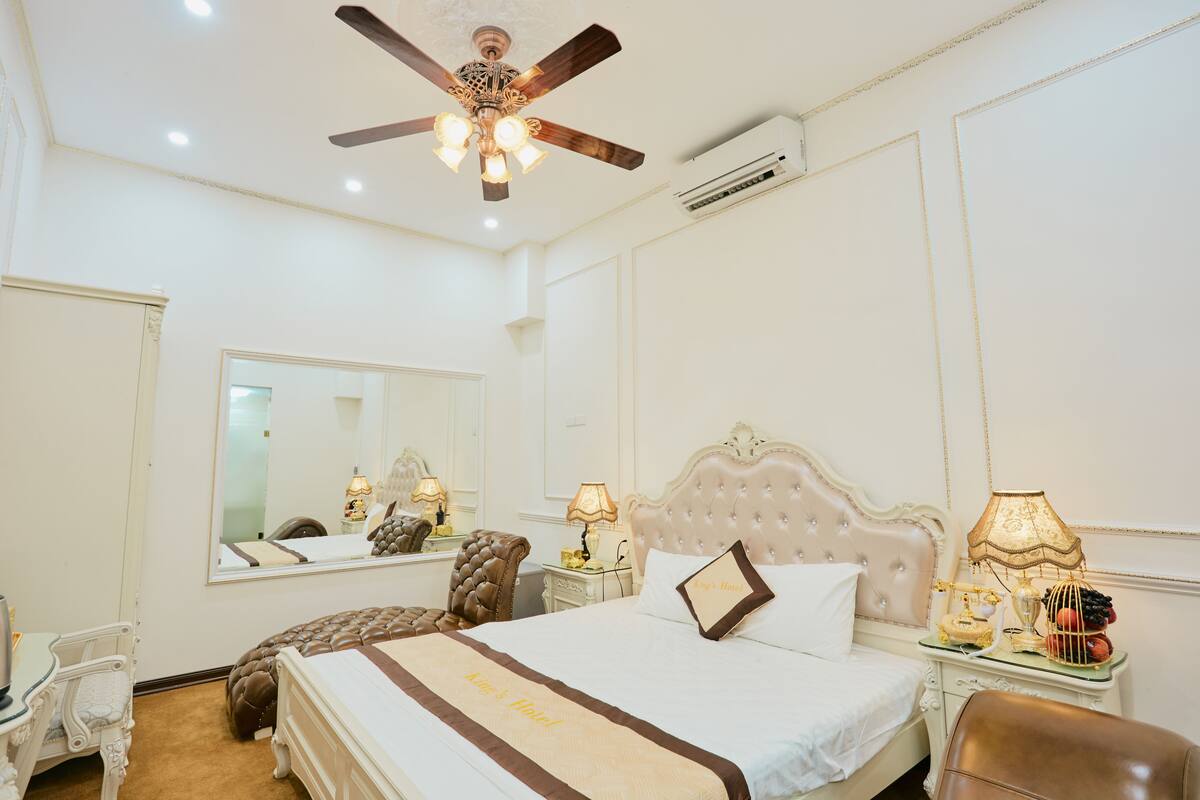 A hotel room with a large bed, a ceiling fan, a mirror, a desk, and a chair.
