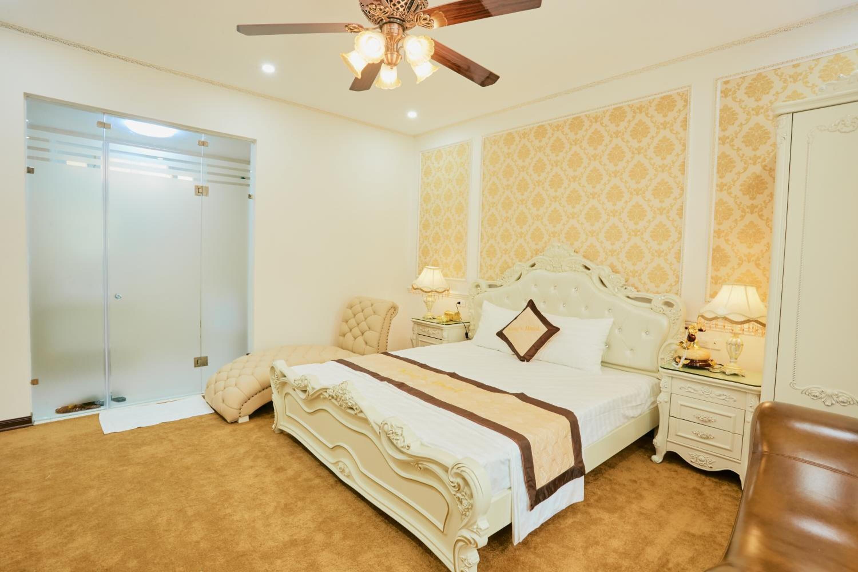 A bedroom with a large bed, a ceiling fan, a wardrobe, and a nightstand with lamps.