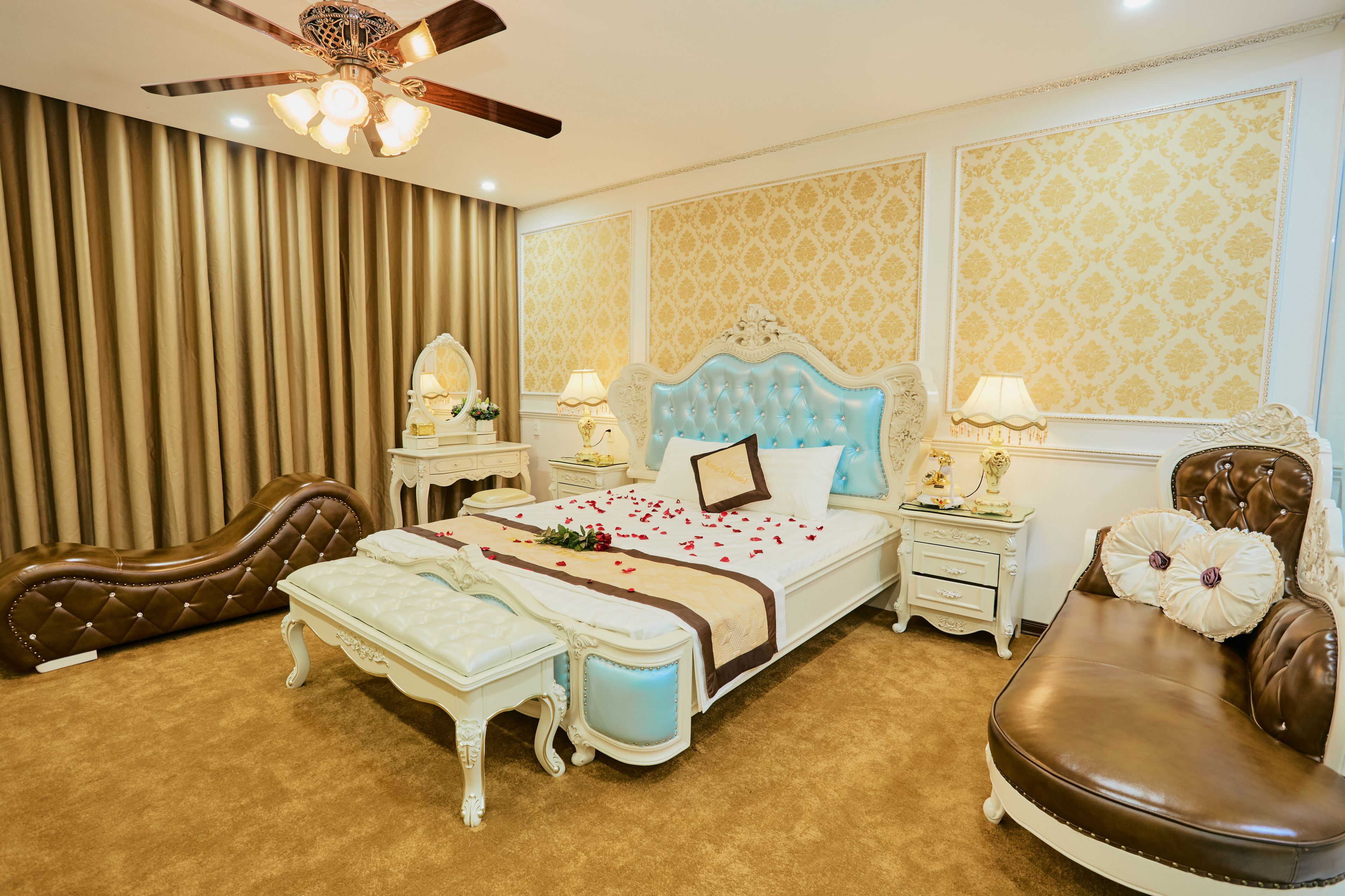 Une chambre à coucher luxueuse, dotée d’un grand lit, d’un coin salon et d’un ventilateur de plafond.