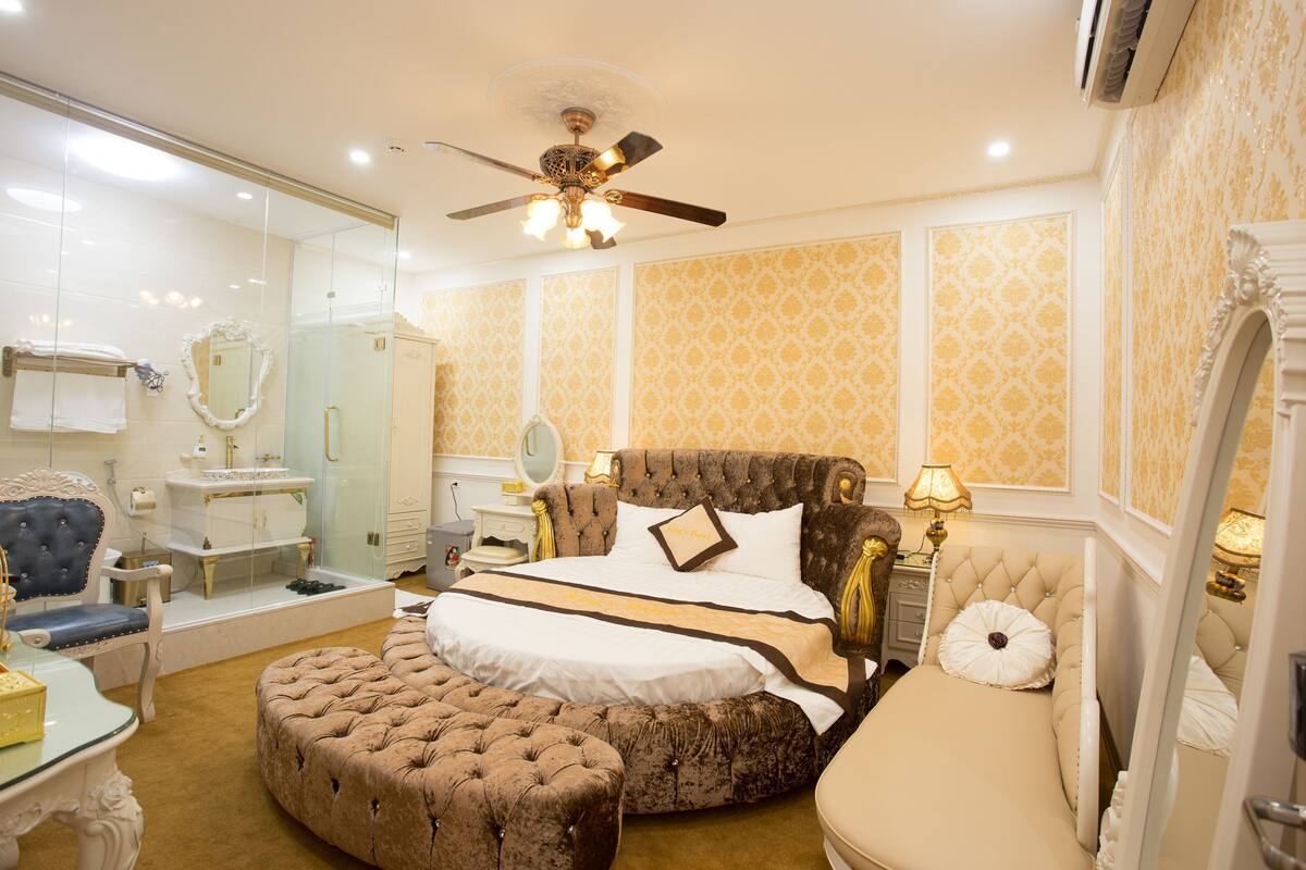 A luxurious bedroom with a large bed, a sitting area, a vanity, and a ceiling fan.