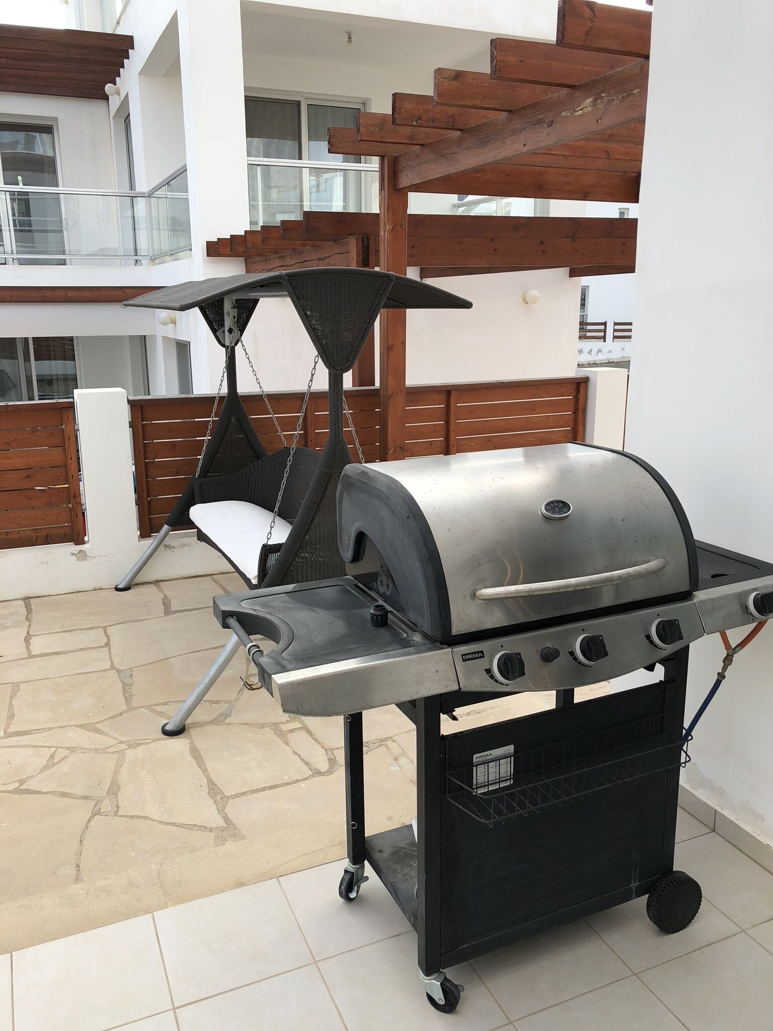 En terrasse med grill, hængekøjsstol og en træpergola.