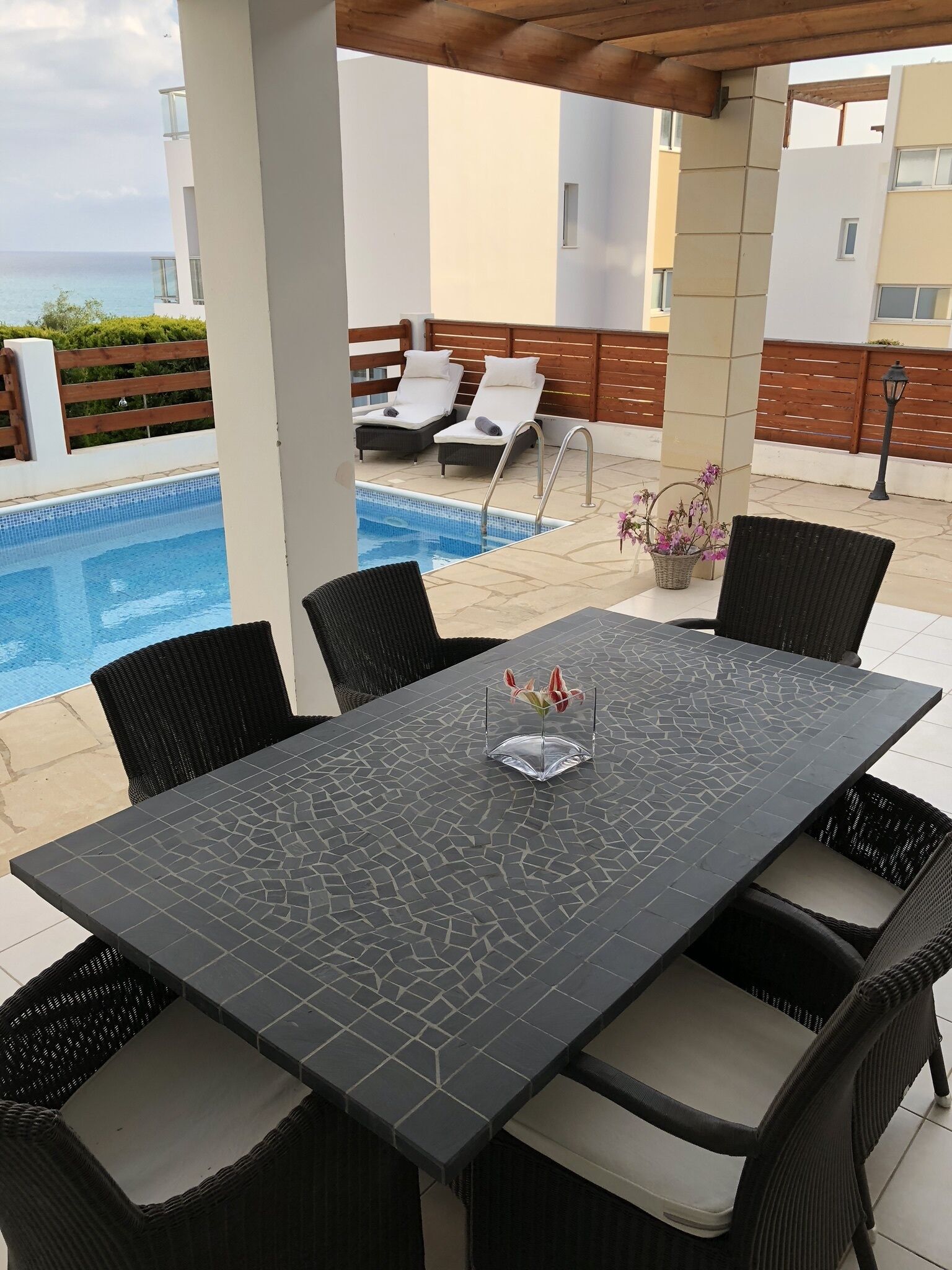 Ein überdachter Außenbereich mit Pool, Liegestühlen und einem Tisch mit Stühlen.