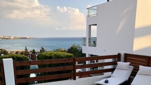 A modern outdoor pool area with a view of the sea, two lounge chairs, and a wooden fence. - Marina Thea Villa No. 11 (Coral Bay)