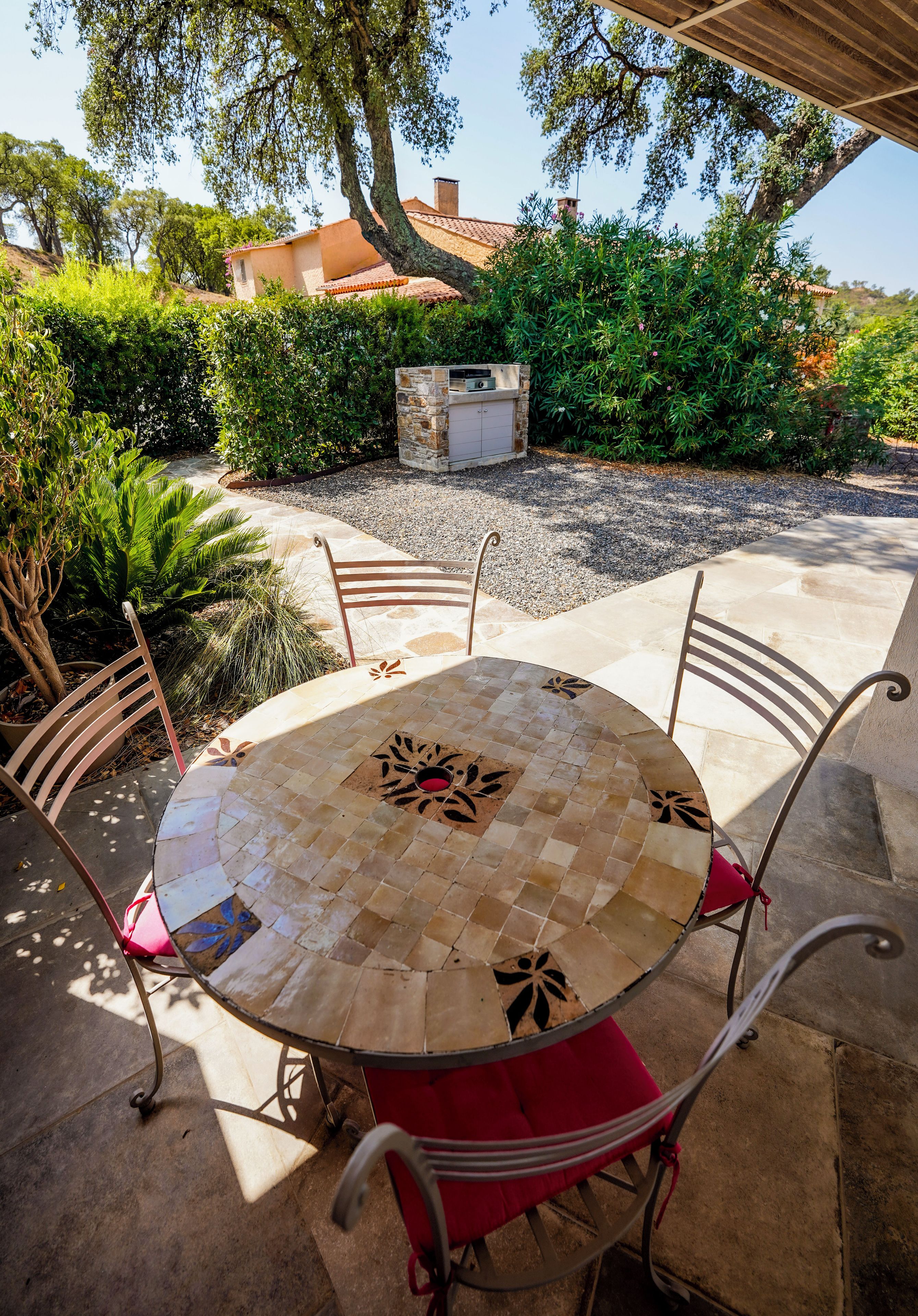 A round outdoor table with a mosaic design, surrounded by metal chairs with red cushions.