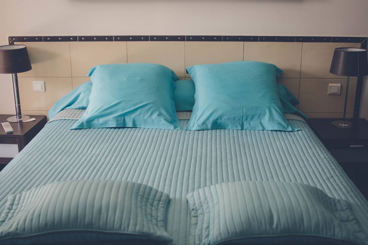 Een bed met hoofdbord, twee bedlampjes en een nachtkastje met een afstandsbediening.