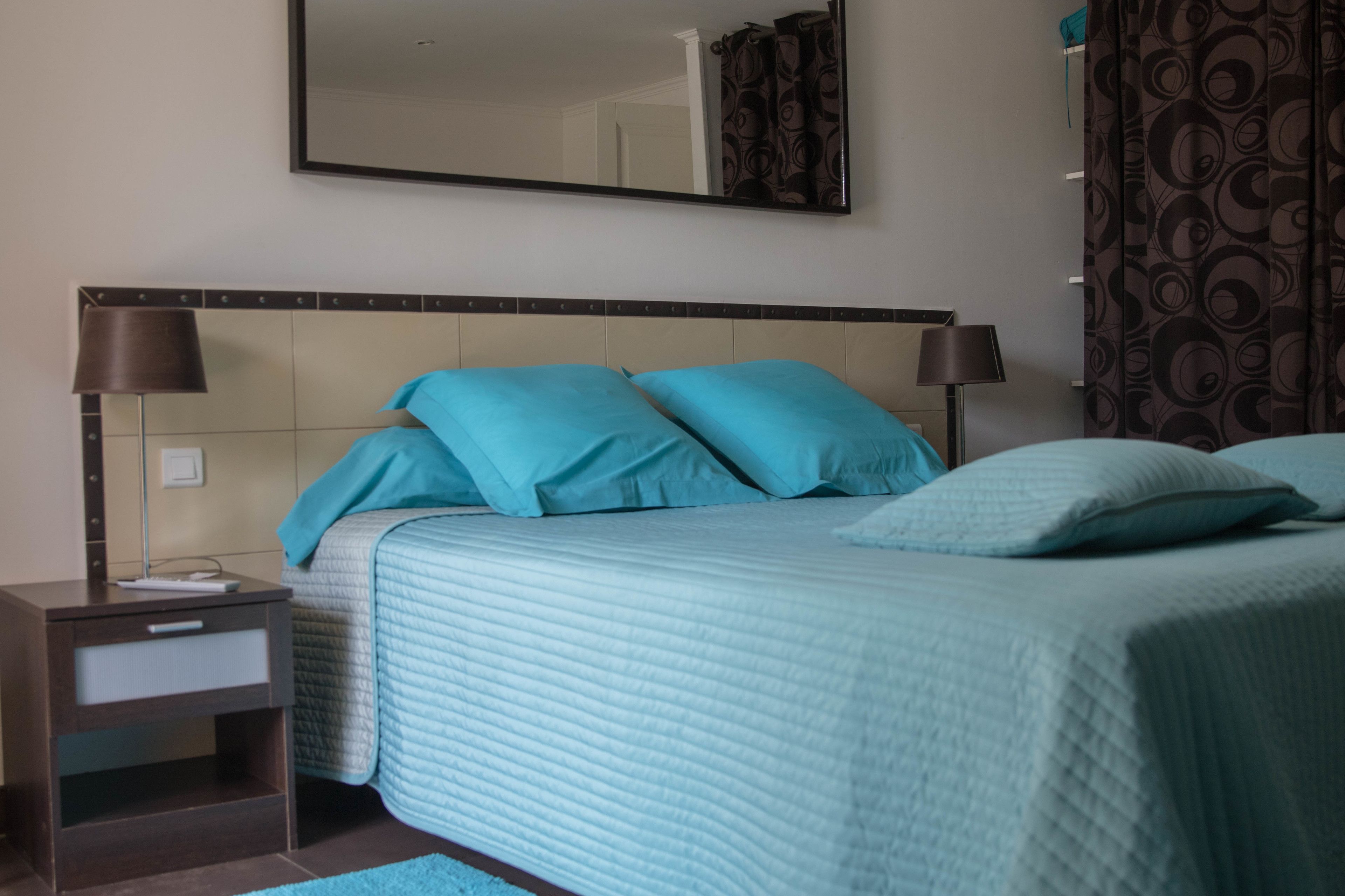 Une chambre à coucher avec un lit, deux tables de chevet, une commode, un miroir et des rideaux à motifs.