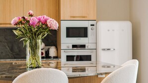 Een moderne keuken met een centraal eiland, twee barkrukken, een vaas met bloemen en inbouwapparatuur.
