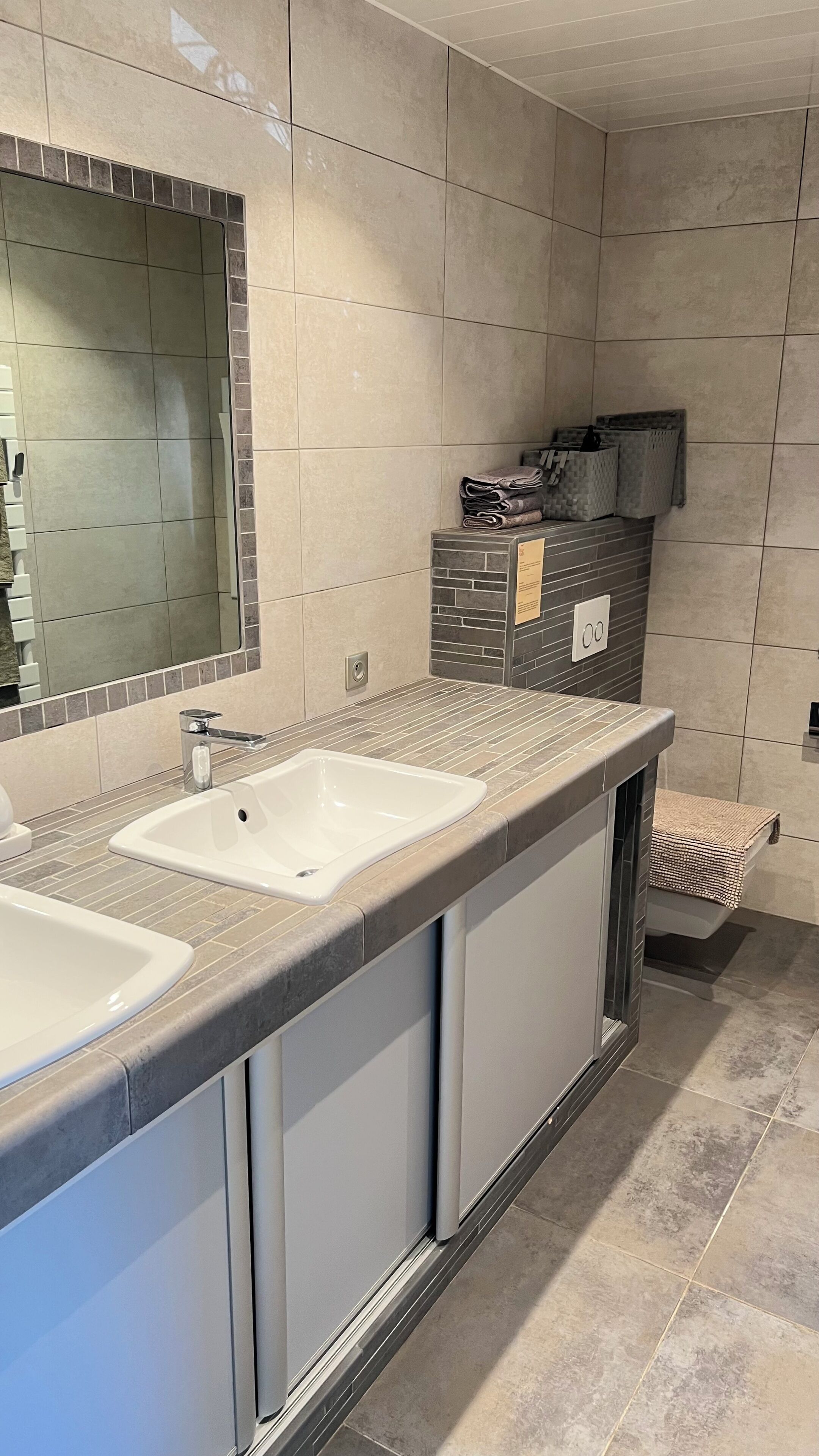 A modern bathroom with two sinks, a large mirror, and a tiled floor.