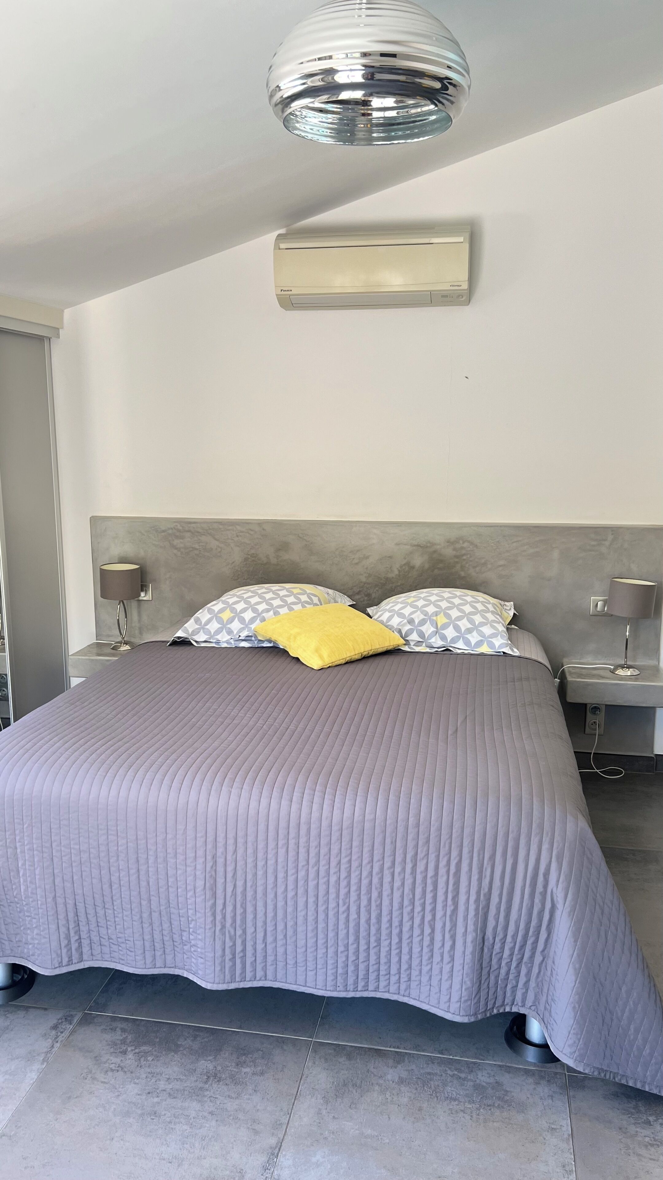 A bedroom with a bed, a wall-mounted air conditioner, and a ceiling light fixture.