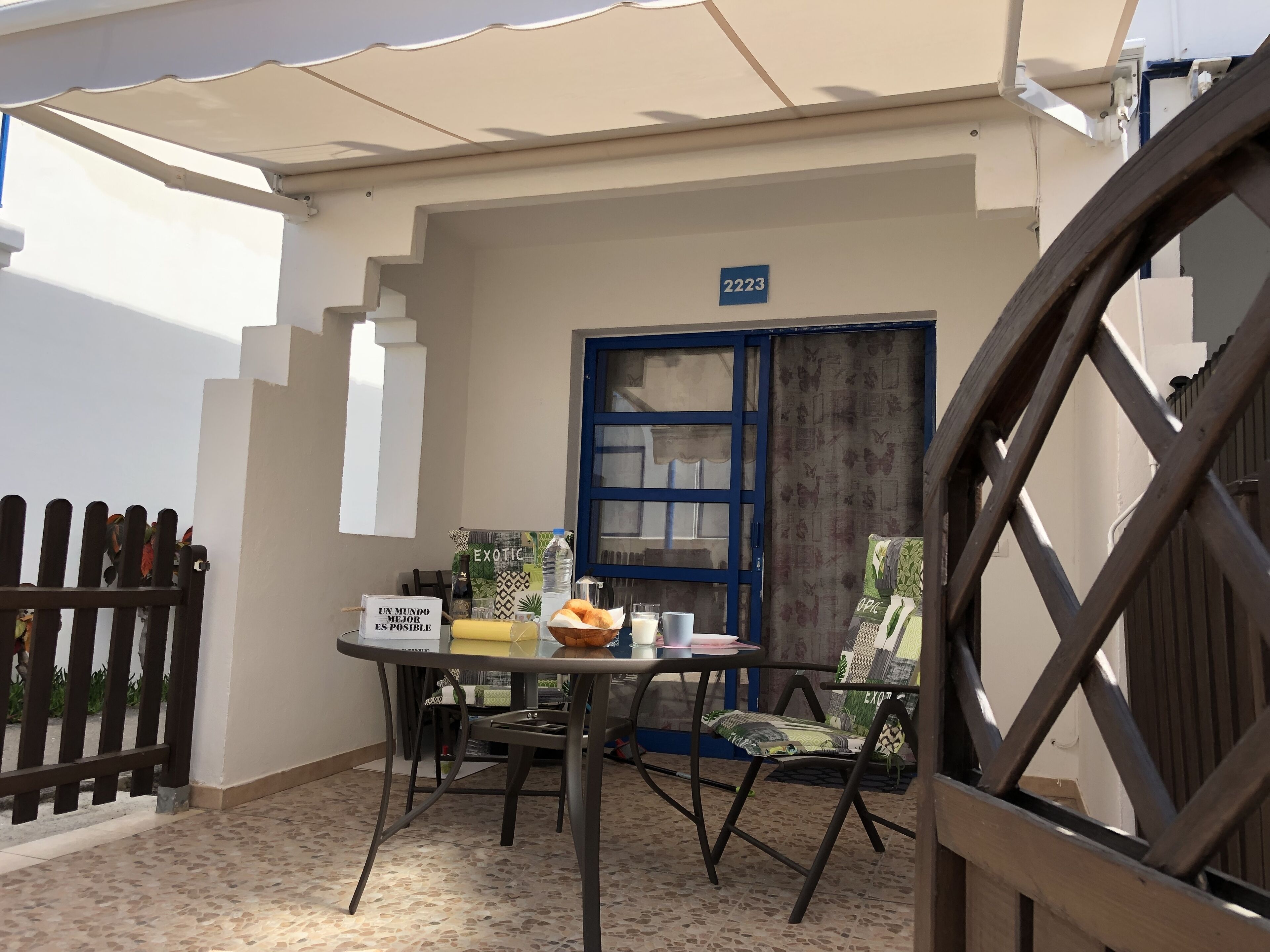 Un petit espace extérieur aménagé avec une table et des chaises, une porte bleue et un panneau indiquant le numéro de l’établissement, placé au-dessus de la porte.