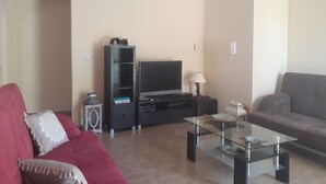 Ein Wohnzimmer mit einem roten Sofa, einem grauen Couchen, einem Glastisch, einer TV-Bank mit einem Flachbildfernseher und einer Lampe.