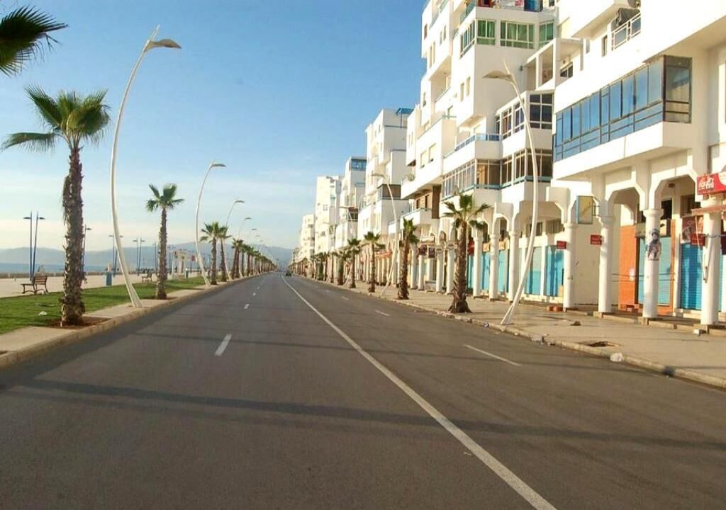 A street lined with palm trees and white buildings with balconies.