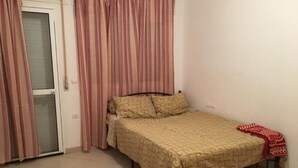 A single bed with a patterned bedspread, a red throw blanket, and a window with curtains. - Residence Chems Corniche Martil 3917 (Martil)