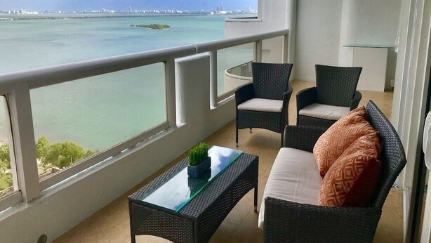 Een balkon met uitzicht op zee, rieten meubels en een glazen tafel.