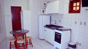 Une cuisine compacte avec un réfrigérateur blanc, un four à micro-ondes, une cuisinière et un évier. On y trouve une petite table à manger avec des tabourets.