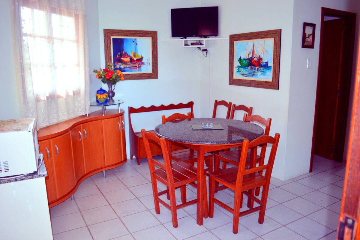 Un coin repas comprenant une table ronde et six chaises, un buffet en bois et deux tableaux accrochés au mur.