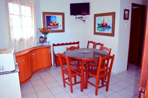 Uma área de refeições com uma mesa redonda e seis cadeiras, um armário de madeira e duas pinturas na parede.