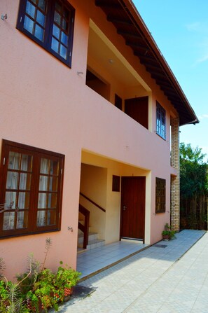 Uma casa de dois andares com varanda, escadaria e porta frontal.