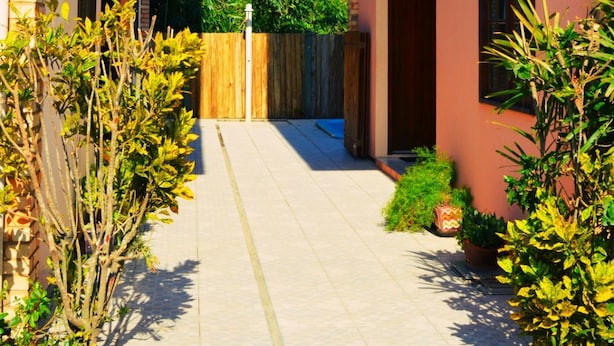 Un étroit passage entre deux bâtiments, bordé d’une clôture en bois et de plantes en pot.