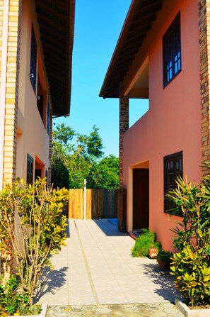 Un étroit passage entre deux bâtiments, bordé d’une clôture en bois et de plantes en pot.