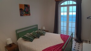 Ein Schlafzimmer mit einem Bett, einem Nachttisch, einer Lampe, einem Fenster mit Vorhängen und einem Bild an der Wand.