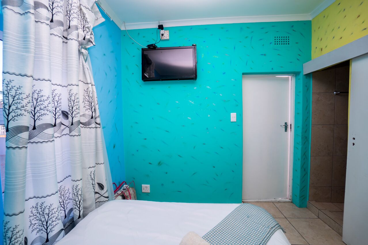 A bedroom with a bed, a television mounted on the wall, and a door.