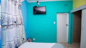 A bedroom with a bed, a television mounted on the wall, and a door.