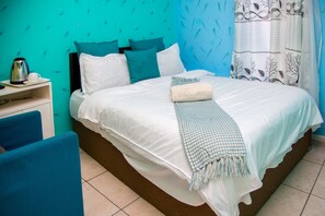 A neatly made bed with a white and blue checkered throw blanket, a white pillow, and a teal pillow. - Annex Lodge (Cape Town)