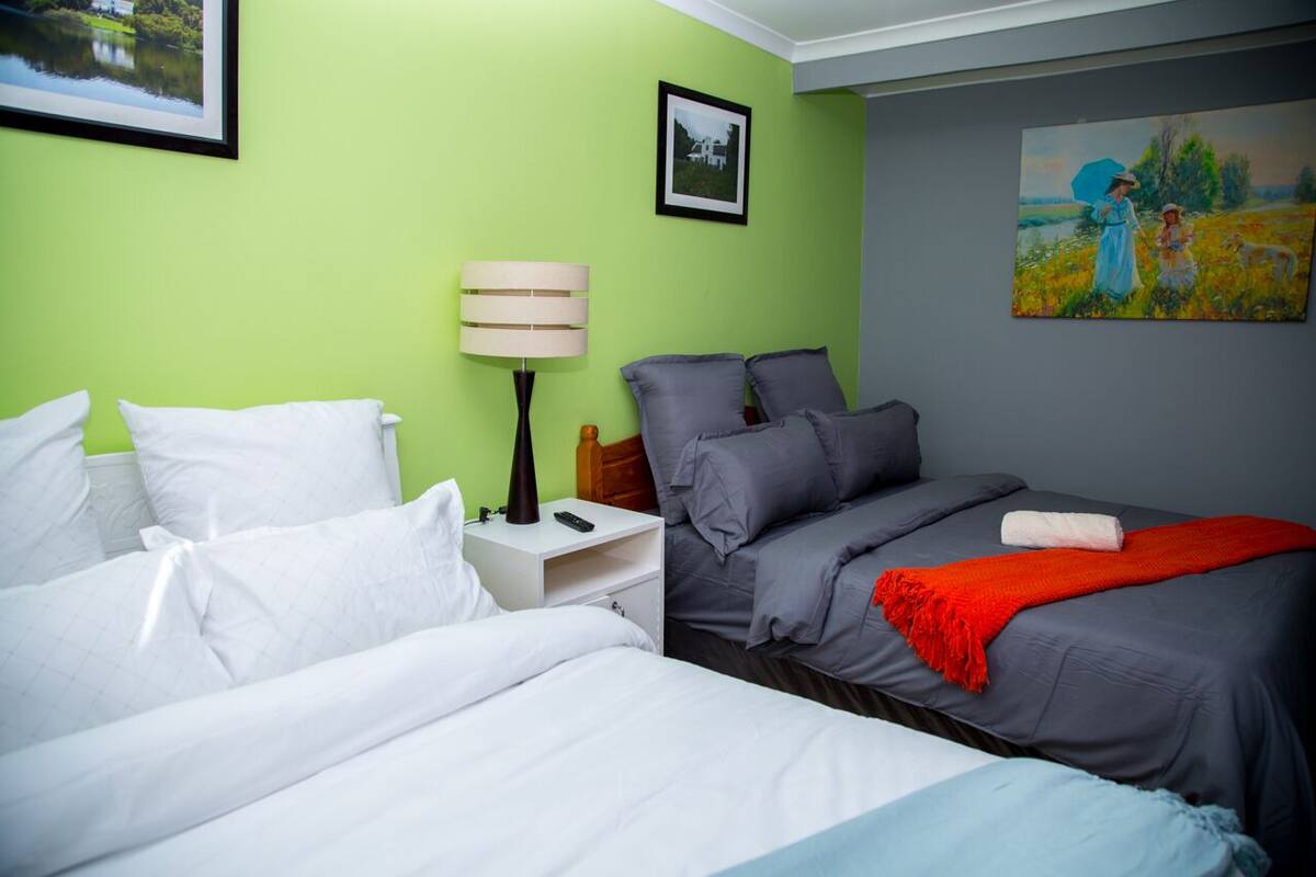 Una habitación de hotel con dos camas, una mesita de noche, una lámpara y obras de arte en las paredes.