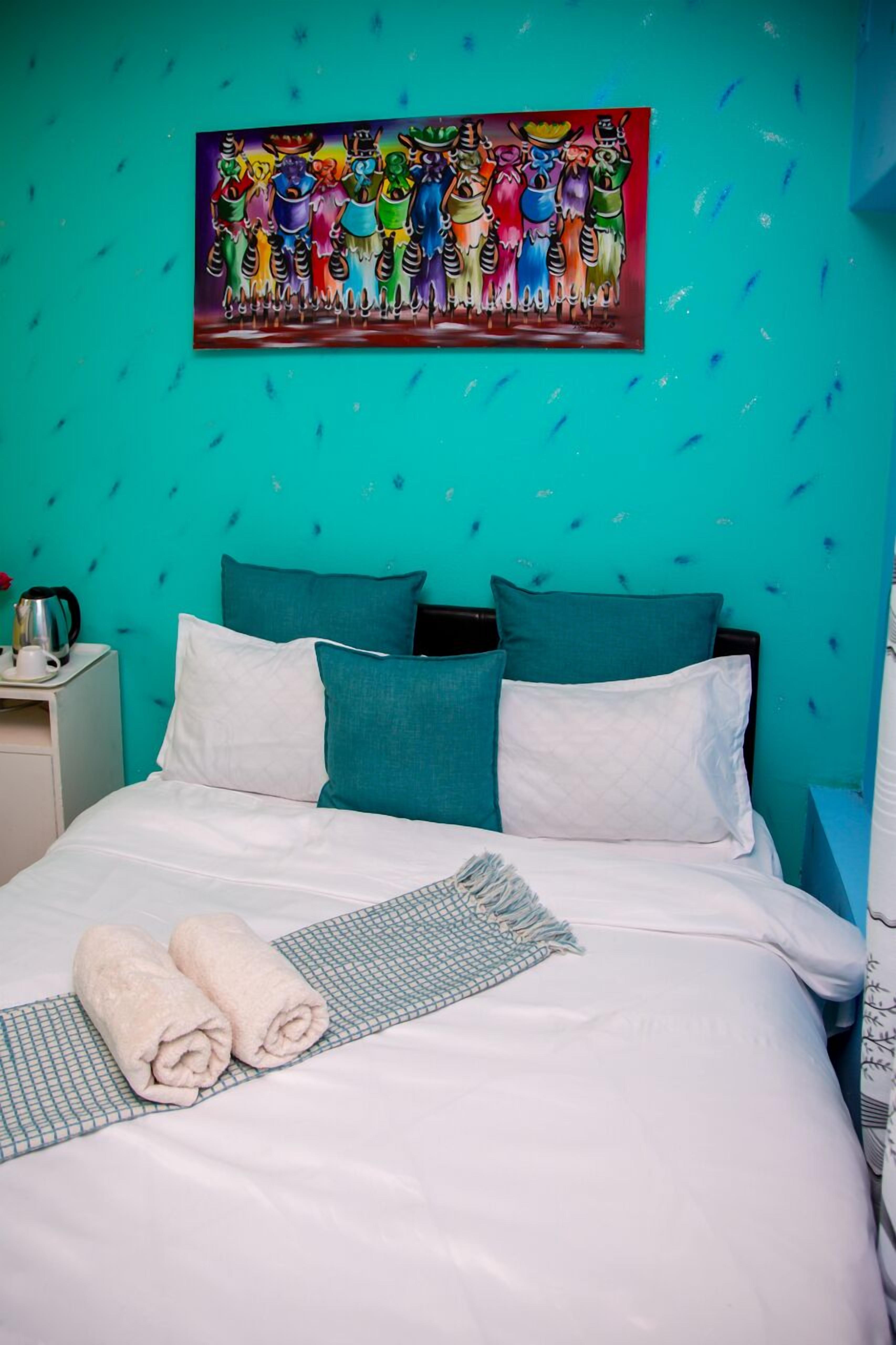 Una camera d'albergo con una parete color verde acqua, un letto con biancheria da letto bianco e verde acqua e un quadro colorato sopra il letto.