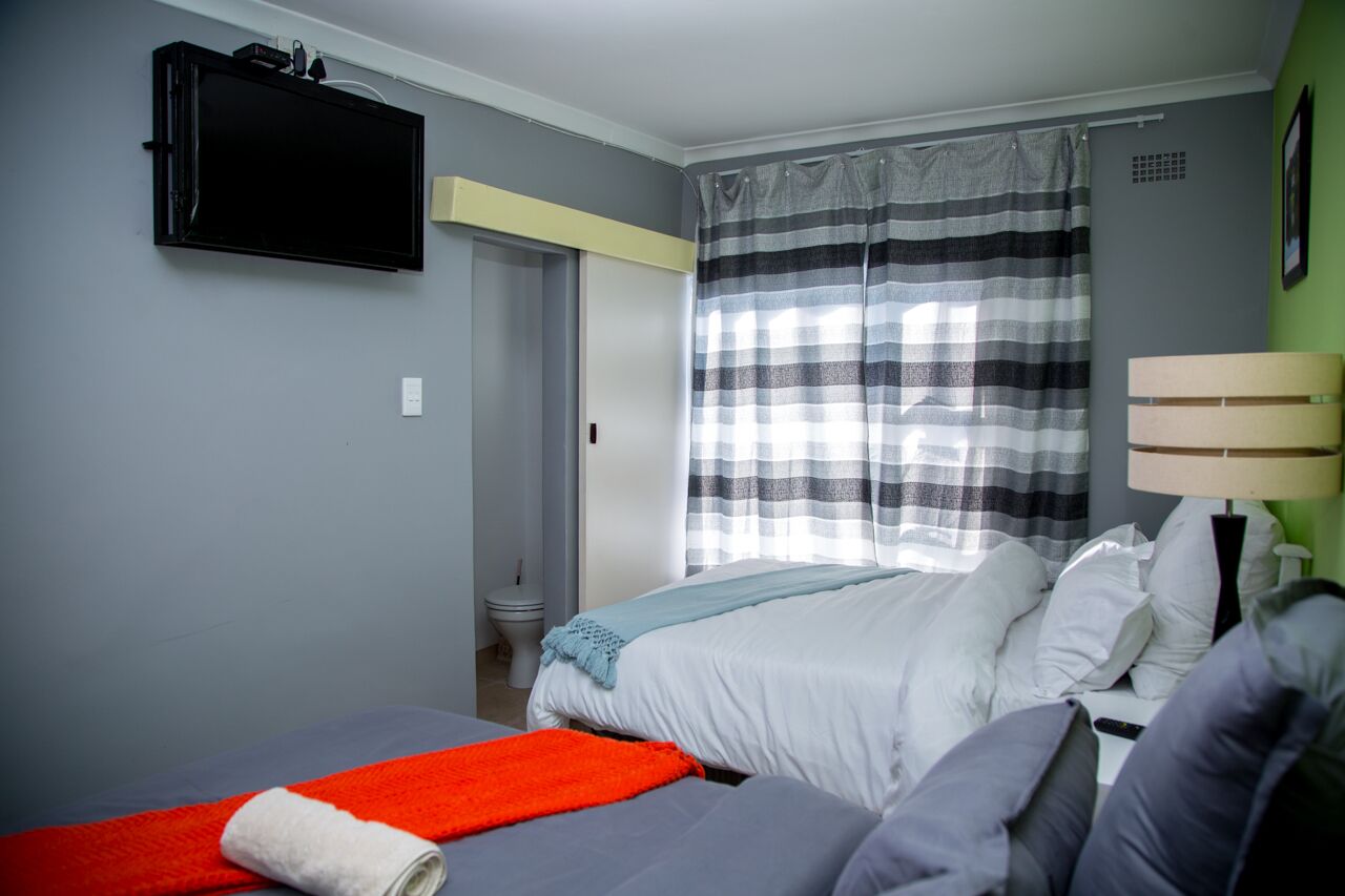 Un dormitorio con cama, una mesita de noche con lámpara, un televisor en la pared y una ventana con cortina a rayas.