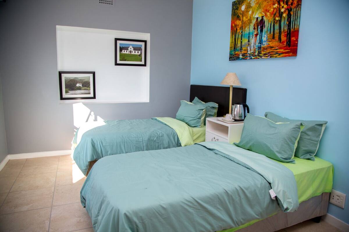 Un dormitorio con dos camas, una mesita de noche, una lámpara y un cuadro en la pared.