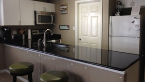 A kitchen with a black countertop, stainless steel appliances, and two green stools.