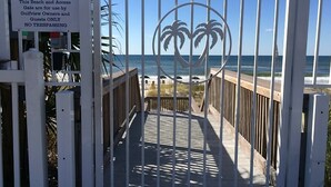 A gated beach access area with a palm tree design, a wooden walkway, and a view of the ocean.