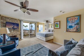 Quarto com cama, ventilador de teto, varanda e vista, e um quadro na parede.