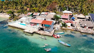 Vista aérea de un pueblo costero con casas de techo de paja, un muelle y aguas turquesas cristalinas.