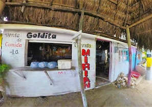 A small, rustic food stall with a thatched roof, labeled 'Goldita' and 'Tenda Mirian.'