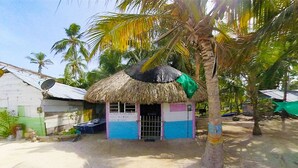 A small, single-story building with a thatched roof, painted in blue and white, surrounded by palm trees and a sandy ground. - Puerto Caracol Isla Múcura (Isla Mucura)