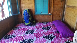 A room with a bed covered in a floral-patterned bedspread, a purple pillow, and a blue and yellow backpack on the bed. - Puerto Caracol Isla Múcura (Isla Mucura)