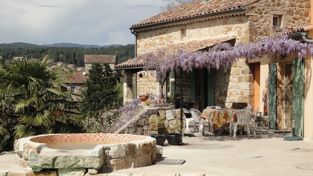 Un bâtiment en pierre avec un toit en tuiles, des places assises à l’extérieur et une piscine.