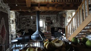 Une pièce rustique avec un mur en pierre, des poutres en bois, une grande cheminée et un escalier.