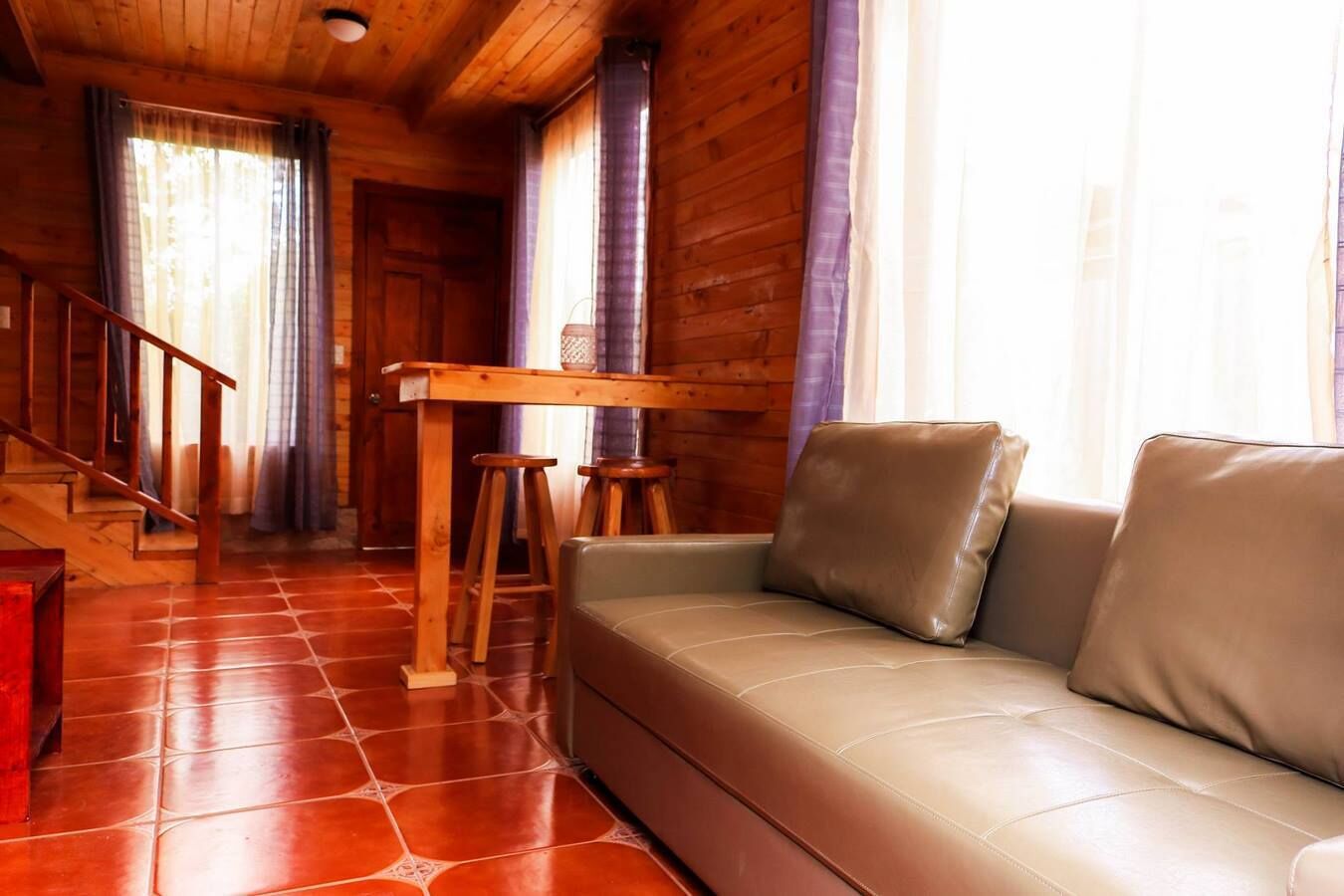 Een houten cabinestijl interieur met een bank, een houten tafel en krukken.