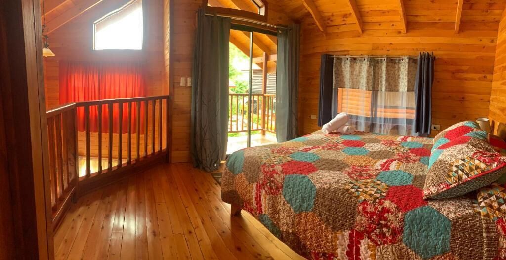 Un dormitorio de cabaña de madera con una cama grande, un balcón y vistas al exterior.