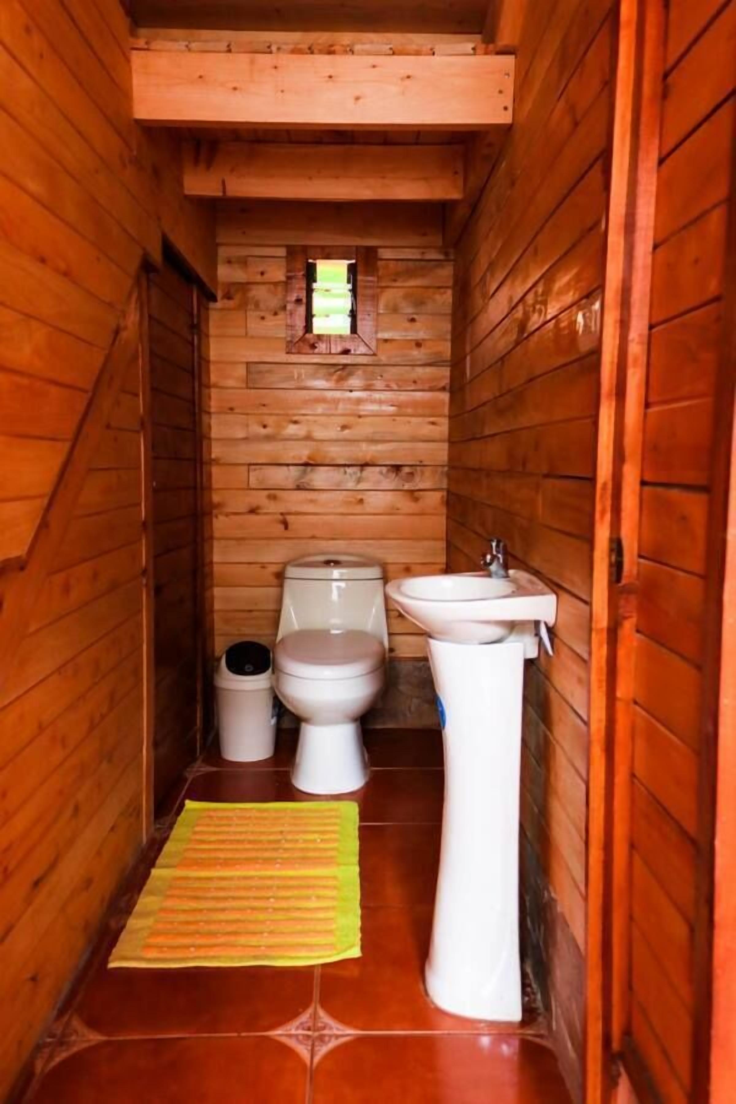 Baño de una pequeña cabaña de madera con inodoro, bidé y lavabo.